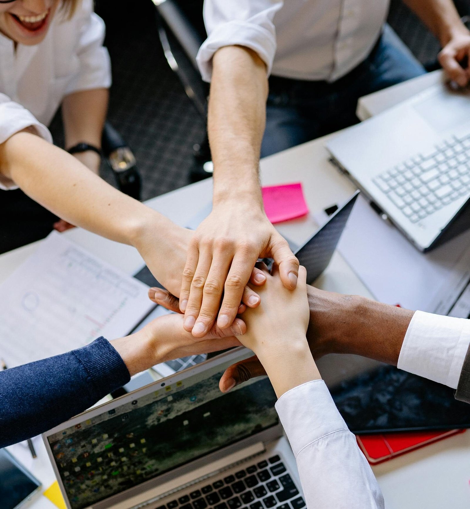 A diverse group of professionals stacking hands over a table symbolizing teamwork and collaboration.